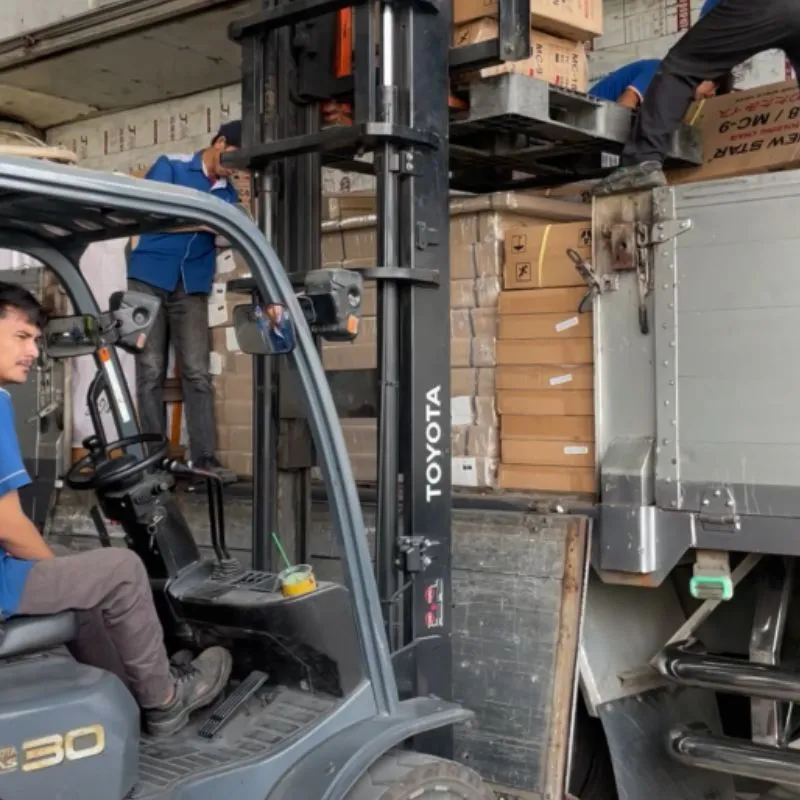 Forklift mengangkat tumpukan karton besar ke dalam truk sebagai ilustrasi proses kirim barang besar ke Kupang.