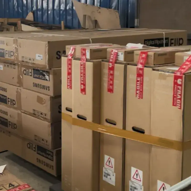Paket elektronik bertanda fragile handling di gudang untuk memastikan keamanan pengiriman.