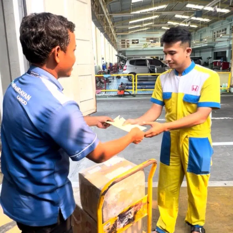 Petugas Papandayan Cargo menyerahkan dokumen kepada teknisi bengkel saat proses pengiriman sparepart, ilustrasi layanan tarif kirim sparepart dan printing.