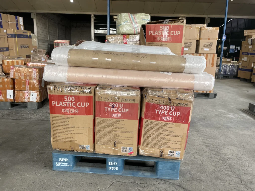 Proses handling dan packing barang di gudang Papandayan Cargo dengan kardus dan gulungan barang yang disusun rapi di atas pallet